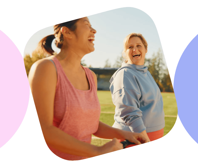 Two women laughing and smiling in a sunlit field, enjoying each other's company on a beautiful day.